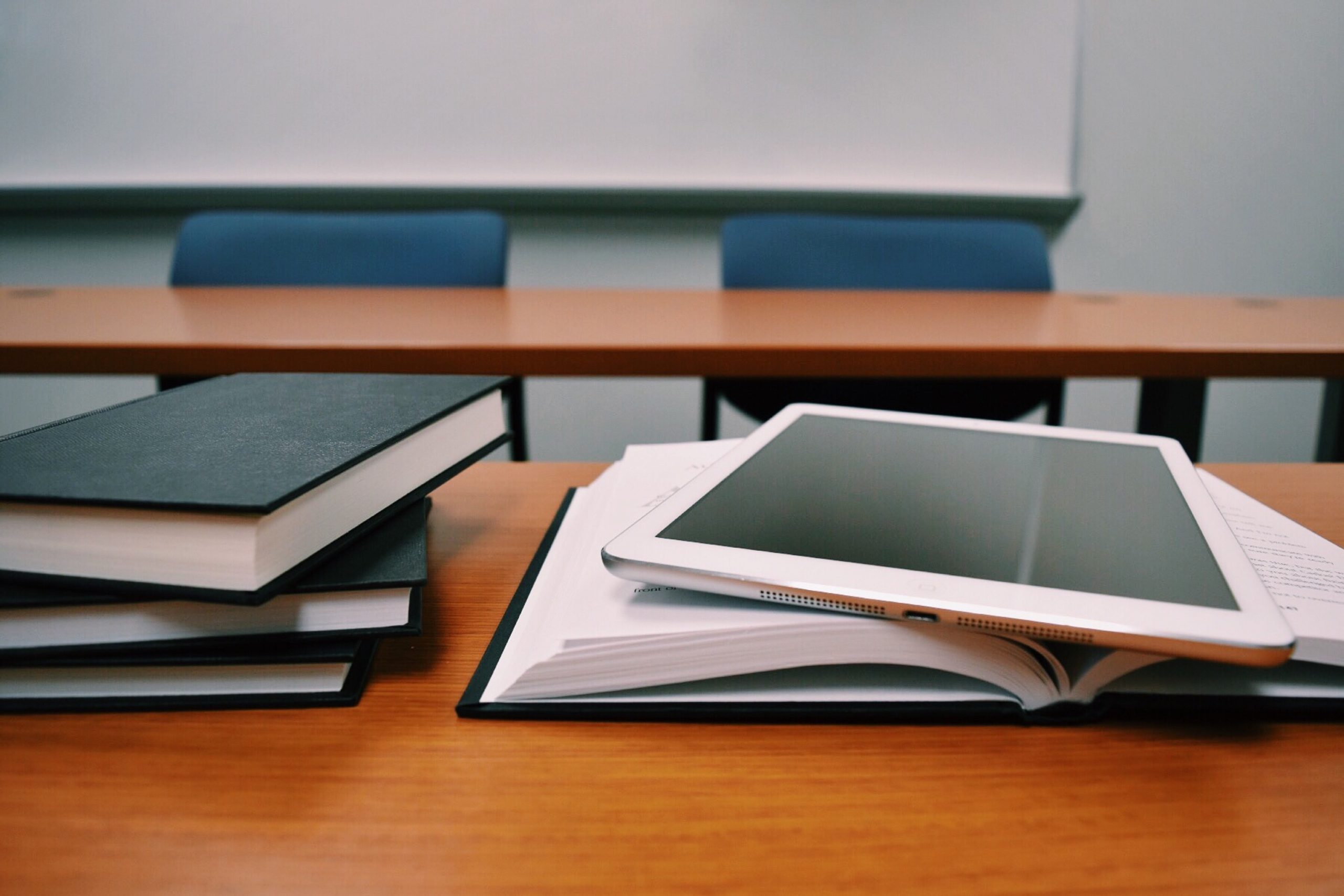 A photo of a stack of books on a classroom table with a tablet on top